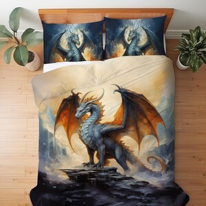Può includere: Un set di biancheria da letto con un design a drago fantasy. Il copripiumino e le due federe presentano un drago blu con ali arancioni su uno sfondo di nuvole e tramonto. Il drago è appollaiato su una roccia.