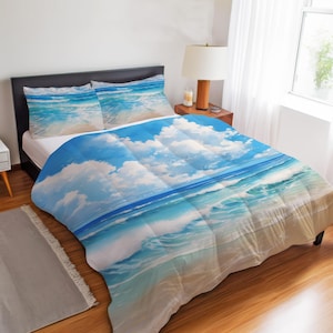 Op de afbeelding: Een beddengoedset bestaande uit een dekbed en twee kussenslopen met een print van een zonnig strand. Het patroon toont lichtblauwe oceaangolven die op een zandstrand spoelen onder een helderblauwe lucht vol met witte wolken.