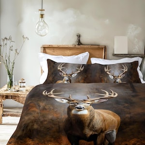Könnte beinhalten: Ein braunes und beiges Bettwäsche-Set mit einem großen Hirsch mit beeindruckendem Geweih. Der Bettbezug und die Kissenbezüge zeigen ein detailliertes Bild des Hirsches vor einem verschwommenen, erdigen Hintergrund. Das Set ist für ein Bett konzipiert.