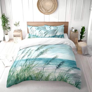 May include: A coastal-themed bedding set with a watercolour design of beach grass and ocean waves in shades of blue and green. The set includes a duvet cover and pillowcases, creating a serene aesthetic. The bed has a wooden headboard.