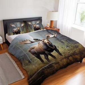 May include: Bedding set with a detailed illustration of a moose in a forest. The set includes a duvet cover and two pillowcases, all with the same wildlife design. The moose is depicted with large antlers and a brown coat.