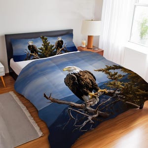 Könnte beinhalten: Bettwäsche-Set mit einem Weißkopfseeadler-Design. Die Bettdecke und die Kissenbezüge zeigen ein detailliertes Bild eines Weißkopfseeadlers, der auf einem Ast sitzt, vor dem Hintergrund einer Berg- und blauen Himmelslandschaft. Die braunen und weißen Federn des Adlers sind sichtbar.