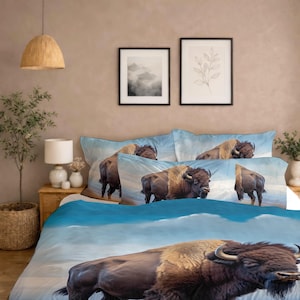 May include: A bedding set featuring a detailed print of bison against a backdrop of a cloudy sky. The duvet cover and pillowcases showcase the majestic animals in shades of brown, tan, and blue, creating a nature-inspired theme.