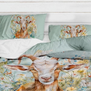 Op de afbeelding: Een lichtblauwe dekbedovertrek en twee kussenslopen met een aquarel illustratie van een geit omringd door bloemen. De geit heeft bruine vacht en grote hoorns. De beddengoedset is ontworpen voor een bed.
