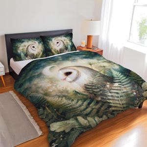 May include: A bedding set featuring a detailed illustration of an owl with a white face and brown and grey feathers, surrounded by ferns and foliage. The set includes a duvet cover and two pillowcases, with a dark green and blue background.