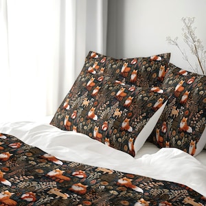 May include: A bedding set featuring a dark charcoal background with a repeating pattern of orange and white foxes interspersed with tan and brown botanical elements, including stylised flowers, leaves, and grasses across the duvet and pillows.