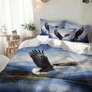 Könnte beinhalten: Bettwäsche-Set mit einer detaillierten Illustration eines Weißkopfseeadlers im Flug über einem See und Bergen. Der Bettbezug und die Kissenbezüge zeigen den Adler mit ausgebreiteten Flügeln vor blauem Himmel und Landschaft.