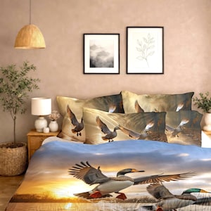 Può includere: Set di biancheria da letto con una vivace scena del tramonto con anatre in volo. Il copripiumino e le federe presentano illustrazioni dettagliate di uccelli acquatici in volo, sullo sfondo di un cielo dorato e acqua.