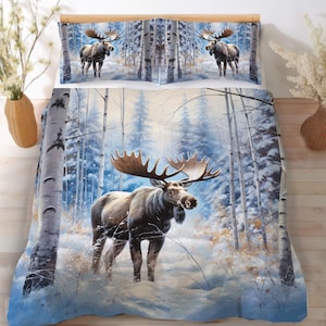 May include: A bedding set featuring a duvet cover and two pillowcases with a winter forest scene. The design displays a large moose with antlers standing in a snowy landscape surrounded by birch trees in shades of blue, white, and brown.