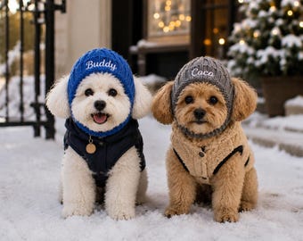 May include: Two dogs wearing knit hats and vests. The white dog wears a blue hat embroidered with the name Buddy and a navy vest. The tan dog wears a grey hat embroidered with the name Coco and a tan fleece vest with black trim.