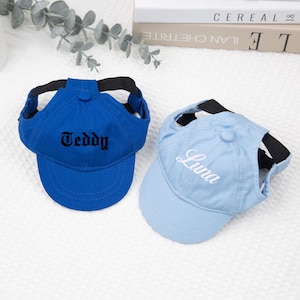 May include: Two pet baseball caps. One is royal blue with "Teddy" in black script. The other is light blue with "Luna" in white script. Both have black straps and a visor.
