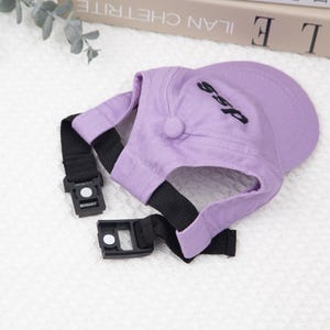 May include: A lavender baseball cap for a pet, featuring a black strap with a buckle and the word "ssp" embroidered in black on the crown. The cap has a button on top and is designed to fit a dog or cat.