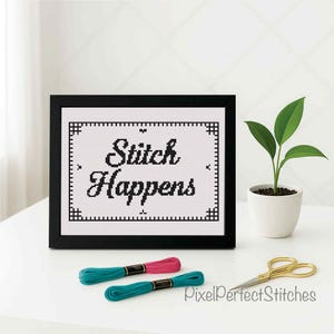 Peut inclure: Un cadre noir contenant une broderie au point de croix avec l'inscription "Stitch Happens" en noir. Deux échevettes de fil à broder, turquoise et rose, et des ciseaux dorés sont devant. Une petite plante en pot est à droite.