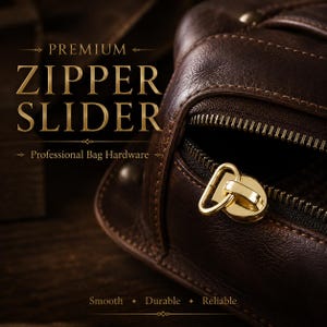 May include: A gold-toned metal zipper slider attached to a dark brown leather bag. The text on the image reads: PREMIUM ZIPPER SLIDER, Professional Bag Hardware, Smooth, Durable, Reliable. The zipper features a polished finish and a loop.