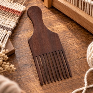 May include: A dark brown wooden hair pick featuring a rounded handle and long, straight, evenly spaced teeth. The comb has a smooth, polished finish and a wide, flat body that tapers from the handle down to the base of the teeth.