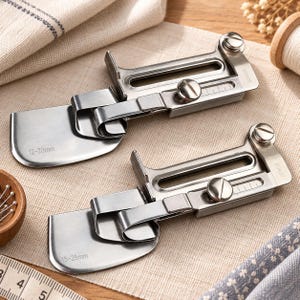 May include: Two silver-toned metal sewing machine presser feet for bias tape binding. The top attachment is marked 12-20mm and the bottom attachment is marked 15-25mm. Both feature adjustable sliding guides, flat metal plates, and screw mechanisms.