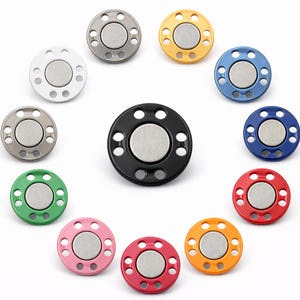 May include: A collection of colorful magnetic snap closures in various colors, including white, gray, yellow, blue, green, pink, red, and black. Each snap has a circular design with a central magnet and surrounding holes.