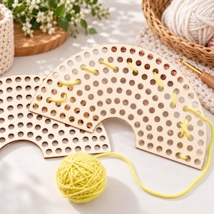 Pode incluir: Duas tábuas de madeira clara em forma de arco-íris com uma grade de orifícios circulares para entrelaçar. Um novelo de fio amarelo brilhante está enfiado nos orifícios de uma das tábuas, com o restante do fio enrolado na superfície.