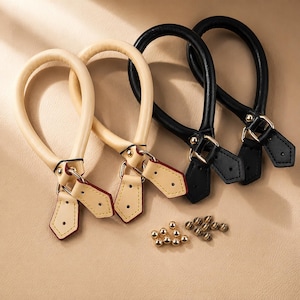 Puede incluir: Dos pares de asas redondeadas para bolso, un par en beige y otro en negro, cada uno con herrajes metálicos dorados, anillas en D y lengüetas de cuero puntiagudas con costuras. Se incluye una pequeña colección de remaches dorados debajo.