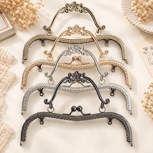 May include: A set of four metal purse frames in varying finishes including antique brass, gold, silver, and gunmetal. Each frame features an arched handle with a central flower motif, a decorative lace-like border, and a dual ball clasp closure.