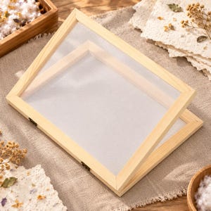 May include: A rectangular wooden frame with a fine white mesh screen stretched across the centre, featuring a hinged design with small metal hardware. The light-coloured wood has a smooth finish and the mesh is taut within the frame structure.