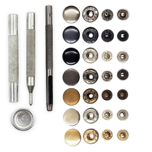 May include: A collection of metal snap fasteners in various colors and sizes, alongside tools for installation. The set includes silver, black, and brass-toned snaps, with a variety of textured and smooth finishes. Tools include a setting tool and a punch.