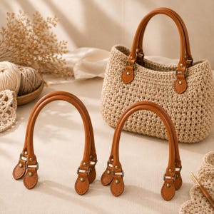 Peut inclure: Un sac à main en crochet beige avec deux anses en similicuir marron clair fixées par des rivets en métal couleur bronze. Deux anses supplémentaires assorties en similicuir marron clair avec des ferrures en métal bronze sont au premier plan.