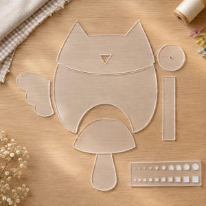 Può includere: Un set di sagome in acrilico trasparente per il fai da te, che include un grande pezzo a forma di gatto, un'ala separata, un pezzo a forma di fungo, un piccolo cerchio, una striscia rettangolare e una guida rettangolare con vari fori circolari e quadrati.