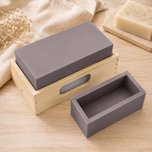 May include: A rectangular light wood box with a cutout handle containing a solid grey silicone block, accompanied by a separate empty rectangular grey silicone mould. The wooden box features visible finger joints at the corners and a smooth finish.