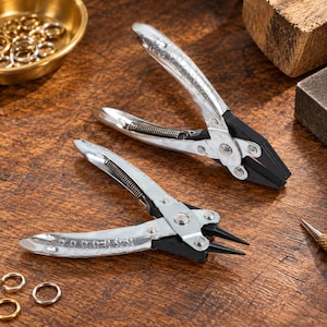 May include: Two metal jewellery pliers with silver-toned handles and black tips. One pair features flat, angled jaws, while the other pair has thin, rounded needle-nose tips. Both tools include a coiled spring mechanism for tension and smooth operation.