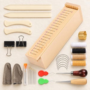 Könnte beinhalten: Ein Lederwerkzeug-Set bestehend aus einer hölzernen Messlehre mit den Zahlen 1-20, zwei Falzbeinen, zwei gebogenen Werkzeugen, zwei schwarzen Büroklammern, einem goldenen Fingerhut, vier Garnrollen, gebogenen Nadeln, Fingerlingen und Ahlen.