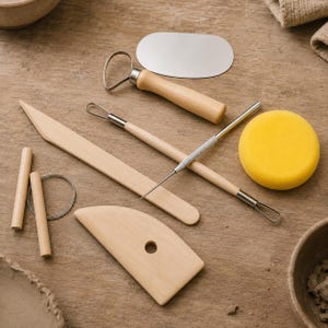 Pode incluir: Um conjunto de ferramentas de cerâmica incluindo uma costela de madeira com um furo, uma ferramenta de modelagem de madeira, uma alça de arame com cabo de madeira, uma ferramenta de metal de ponta dupla, um raspador de metal, dois pinos de madeira e uma esponja amarela.