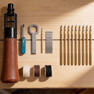 May include: A collection of tools, including a brown leather-wrapped handle, a blue screwdriver, a wrench, needles, and gold-colored rods. Also included are spools of white, brown, and black thread. The tools are arranged on a light wooden surface.