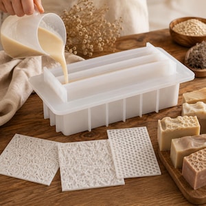 May include: A rectangular translucent silicone soap mold with a removable lid and internal dividers. Three square silicone texture mats with rose, floral, and honeycomb patterns are placed in front of the mold alongside finished soap bars.