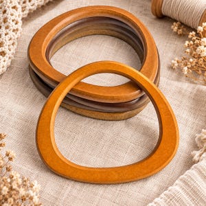 May include: A set of four smooth, rounded, irregular-shaped wooden bag handles in varying shades of brown, ranging from light amber to dark espresso. Each handle features a polished finish and a distinct, organic, non-circular, curved silhouette.
