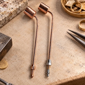 Peut inclure: Deux outils en métal de couleur cuivre avec de longues tiges fines et coudées surmontées de têtes cylindriques. Un outil présente une pointe couleur cuivre, tandis que l'autre possède une pointe métallique argentée pour le travail du métal.