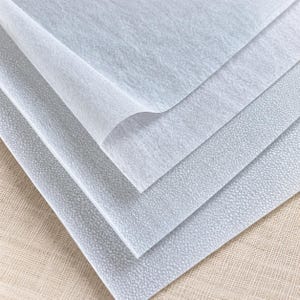 May include: Three stacked sheets of white material. The top sheet is thin, translucent, and fibrous with a smooth surface. The two bottom sheets are opaque, thicker, and feature a distinct, uniform, fine-grained, pebbled texture across the surface.