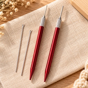 Peut inclure: Deux découseurs en métal rouge avec des poignées texturées argentées et deux lames de rechange fines en argent. Les outils présentent une extrémité pointue et une pointe en forme de fourche pour couper les fils. Design élégant et métallique.