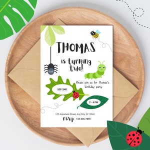 May include: A white invitation card with green leaves and colorful bugs. The text on the card reads "THOMAS is turning two!" with the date "SEP 2ND" and time "2-4 PM". The invitation also includes an address and RSVP information.