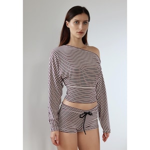 May include: A two-piece striped outfit. The top is off-the-shoulder with long sleeves, and the shorts have a drawstring waist. Both are striped in black and light pink. The outfit is a matching set.