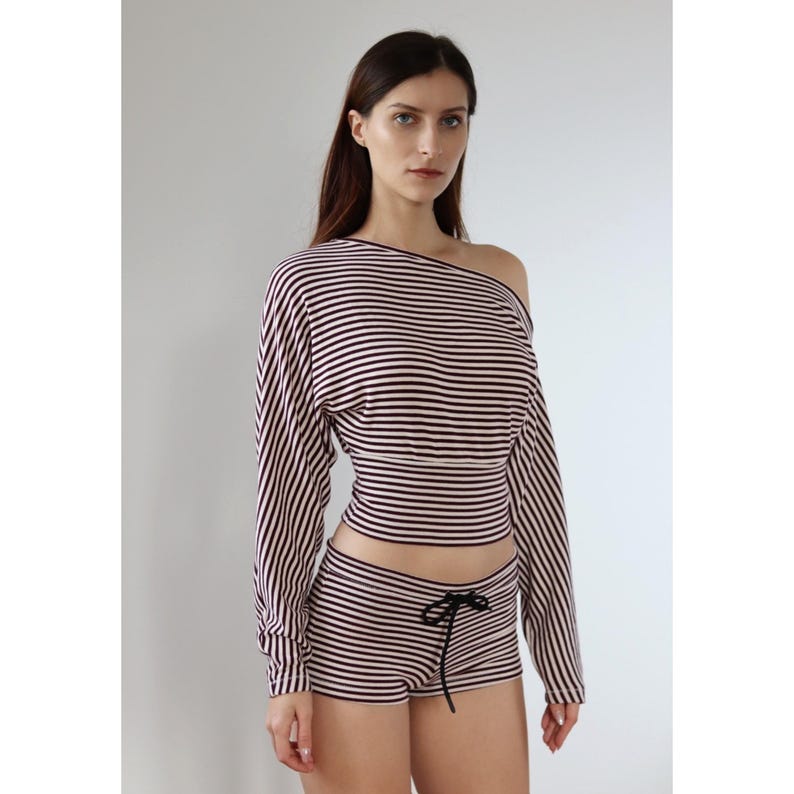 May include: A two-piece striped outfit. The top is off-the-shoulder with long sleeves, and the shorts have a drawstring waist. Both are striped in black and light pink. The outfit is a matching set.