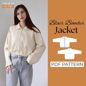 Op de afbeelding: Een beige Blair Bomber Jacket met ritssluiting, gedragen met lichtblauwe jeans. De afbeelding bevat de tekst "Blair Bomber Jacket" en "PDF Pattern". Het logo van The Seam Studio staat in de linkerbovenhoek.