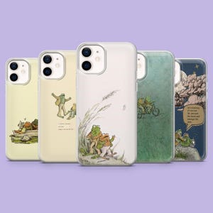 May include: Five phone cases featuring frog illustrations. Designs include frogs on a log, walking, riding a bicycle, and under a starry night sky. The cases are clear, showcasing the illustrations.