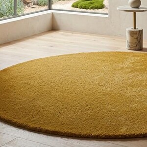 Round mustard wool rug edge detail on wooden floor, handmade tufted minimalist circle carpet texture view