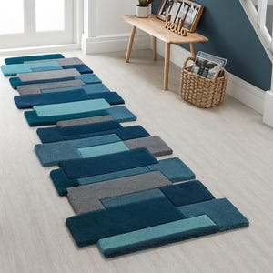 May include: A rectangular, geometric runner rug in shades of blue and gray. The rug features a pattern of overlapping rectangular shapes in various shades of teal, blue, and gray. The rug is placed on a light-colored wooden floor.