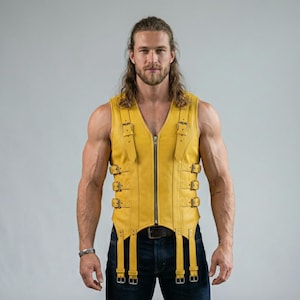 May include: A yellow leather vest with multiple buckles and a front zipper. The vest has a V-neck design and is worn with dark blue jeans. The vest is a bold fashion statement.