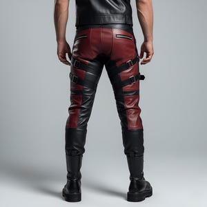 May include: Leather pants featuring a color-blocked design in black and deep red. The trousers include two horizontal zippered pockets on the back, multiple adjustable black leather straps with silver-toned metal buckles, and a fitted silhouette.
