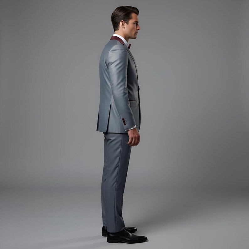 May include: A gray suit with a burgundy lapel and bow tie. The suit has a two-button closure and is paired with black dress shoes. The background is a solid gray.