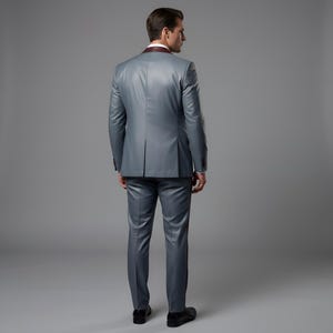 May include: A gray suit with a burgundy lapel and a matching pair of trousers. The suit is tailored and has a classic design. The person is wearing black shoes.