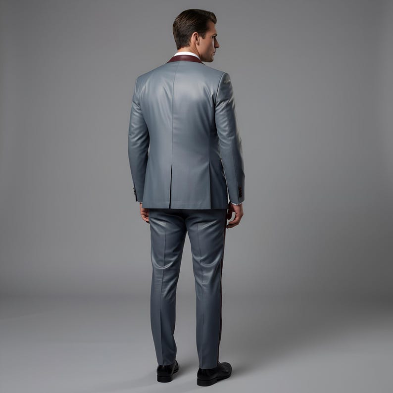 May include: A gray suit with a burgundy lapel and a matching pair of trousers. The suit is tailored and has a classic design. The person is wearing black shoes.
